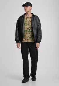 Must must märkbruna bomber-jakk, mille all on kamuflaažimustriga särk, kokku sobitatud mustade pükste ja mustade tossudega. Märgatavaid accentsid ei ole.