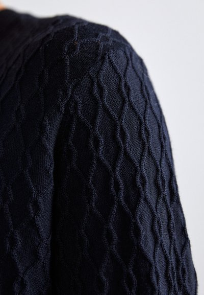 Navy-gestricktes Kleidungsstück mit einem strukturierten Diamantmuster, das aufwendige Stiche und einen weichen, atmungsaktiven Stoff präsentiert.