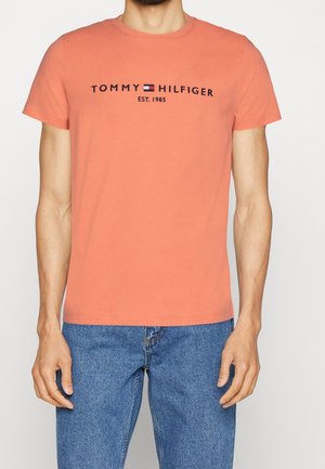 Triko s krátkými rukávy v korálové barvě vyrobené z bavlny, s černým potiskem loga "TOMMY HILFIGER EST. 1985" na přední straně.