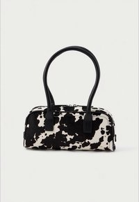 Sac à main imprimé motifs vache noir et blanc avec une forme structurée, un matériau doux au toucher et deux anses en cuir noir. Fermeture éclair sur le dessus.