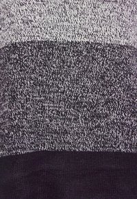 Stickad tröja med ett randigt mönster i växlande nyanser av grått och svart, med en texturerad yta och en enfärgad svart nederdel.