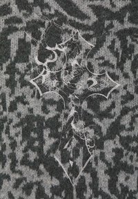 Grijze gebreide trui met een zwart abstract patroon. Heeft een ingewikkeld wit ontwerp dat lijkt op een kruis met florale elementen.