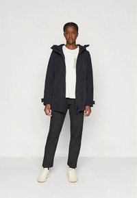 Juoda neperšlampama striukė su gobtuvu, priekiniu kišeniu ir užtrauktuko uždarymu. Derinama su balta marškinėle ir juodomis kelnėmis.