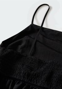 Czarna sukienka z cienkimi ramiączkami, marszczonym gorsetem i detalami z marszczonego materiału. Materiał wydaje się lekki i teksturowany.