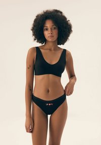 Czarny stanik i pasujące figi wykonane z gładkiego materiału. Stanik ma szerokie ramiączka i głęboki dekolt. Figi mają niską talię z wzorem w serduszka.