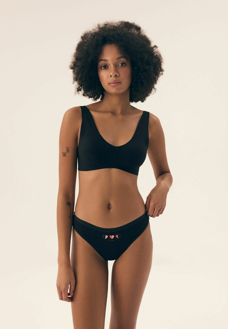 Czarny stanik i pasujące figi wykonane z gładkiego materiału. Stanik ma szerokie ramiączka i głęboki dekolt. Figi mają niską talię z wzorem w serduszka.