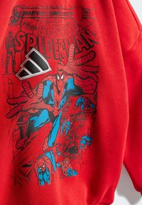 Sweatshirt rouge avec un graphique de Spider-Man en bleu et noir, accompagné d'un patch du logo Adidas en noir et blanc. Tissu doux et texturé.