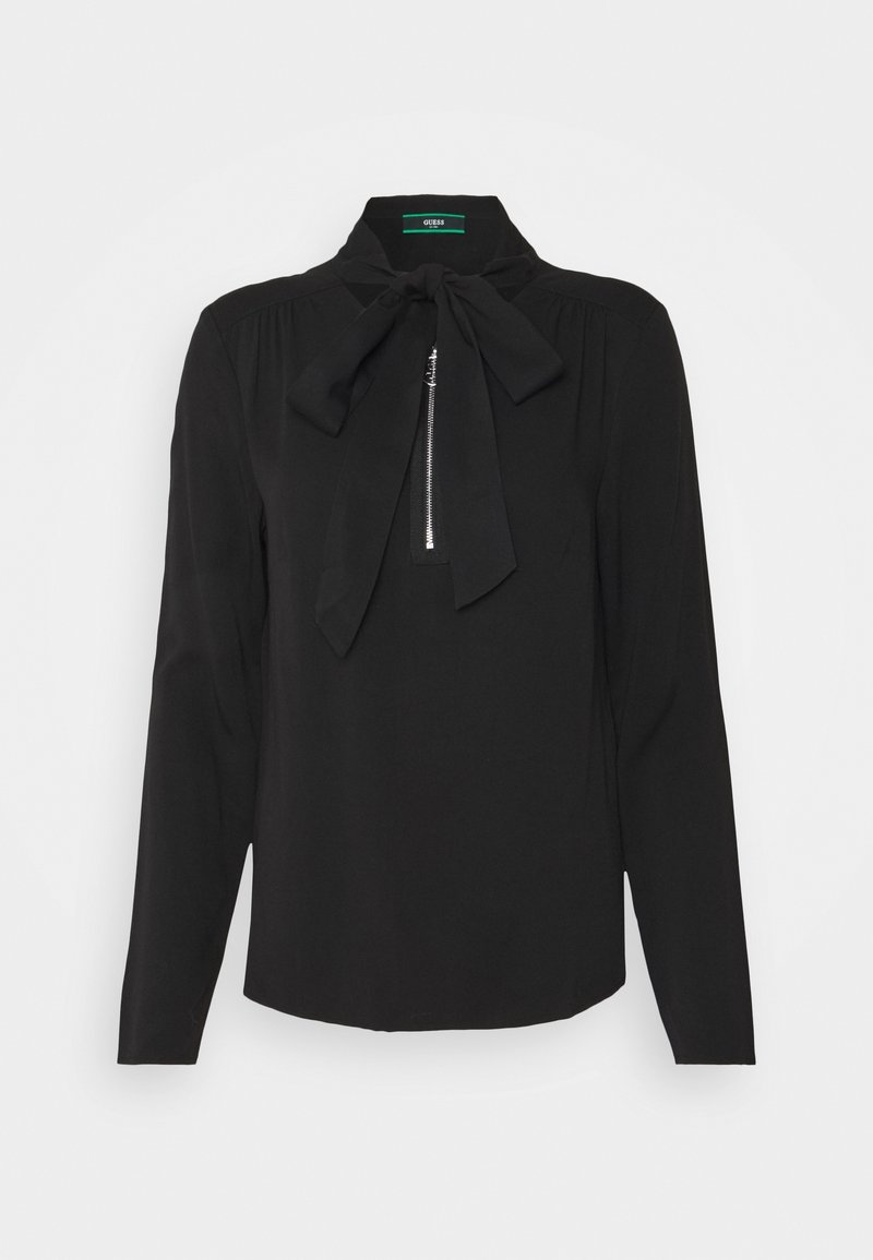 Blouse noire à manches longues avec un col à nœud. Détail de zip à l'avant. Tissu lisse avec une coupe légèrement ample et un ourlet arrondi.