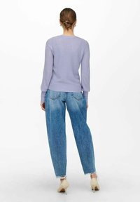 Lila ribbad tröja med långa ärmar, i kombination med högmidjade, löst sittande blå jeans och beige klackskor. Vit bakgrund.