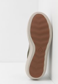 Sneaker sostenibile con una parte superiore verde oliva texturizzata, suola in gomma marrone e un sottopiede beige sagomato con dettaglio del logo.