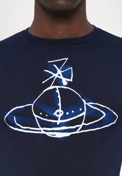 Marineblaue T-Shirt mit einem grafischen Design, das eine weiße und blaue Illustration eines Planeten mit Ringen zeigt, ergänzt durch dynamische Linien und Details.