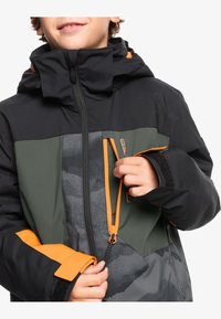 Veste noire et verte avec des accents orange. Comprend une poche zippée, une section en tissu à motifs et un col montant.