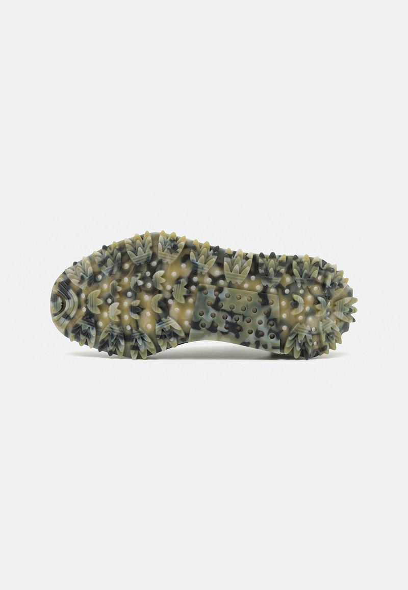 Suela de un zapato con una superficie de goma texturizada y picos en múltiples direcciones, principalmente en tonos de verde oliva y negro.