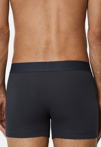 Schwarze gerippte Boxershorts mit einem glatten Bund, die durch ihre glatte Textur und minimalistisches Design bestechen. Die Rückansicht zeigt den anschmiegsamen Schnitt.