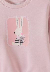 Tissu rose pâle avec un lapin cartoon imprimé portant une chemise rayée et un grand nœud, encadré par une bordure rectangulaire rose douce.
