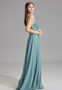 Abito da sera teal con un corpetto aderente e scintillante adornato di perline, spalline sottili e una gonna fluida realizzata in tessuto morbido e leggero.