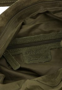Olivengrünes Wildlederinterieur einer Tasche mit einem Reißverschlusstaschen. Ein Lederschild trägt die Aufschrift "MENEZIA" und "Echtes Leder." Weicher, strukturierten Stoff.