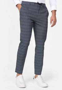 Marineblaue karierte Hose mit Kordelzug, tailliertem Schnitt und schmal zulaufendem Bein, kombiniert mit weißen Sneakern.