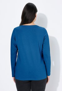 Niebieska koszula z długim rękawem wykonana z gładkiej tkaniny, z okrągłym dekoltem i luźnym krojem, zestawiona z ciemnymi spodniami.