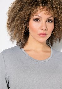 T-shirt a maniche corte grigio a righe con scollatura rotonda, realizzato in tessuto morbido, con dettagli di cucitura sottili. Modello con capelli ricci che indossa orecchini a cerchio.