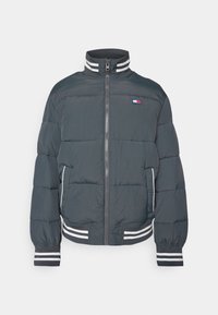 Chaqueta acolchada en gris oscuro con cierre de cremallera, cuello alto y rayas blancas contrastantes en los puños y el dobladillo. Cuenta con un parche de logo.