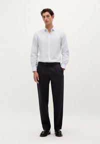 Weißes Hemd mit Knopfleiste, dunkle Hose und schwarze Schuhe. Das Hemd hat einen klassischen Kragen und lange Ärmel; die Hose ist mit Falten und geradem Schnitt.