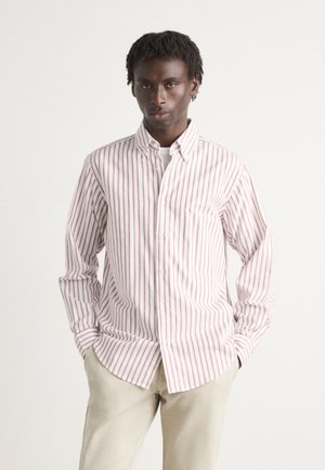 Witte shirt met dunne rode verticale strepen, met knoopsluiting bij de kraag, lange mouwen en een gebogen zoom. Draag het met lichtgrijze broek.