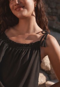 Black top featuring a smocked neckline and adjustable straps with tassel accents, made from lightweight, flowing fabric.