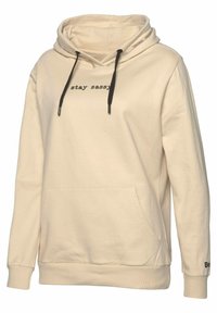 Sudadera con capucha de algodón beige con un bolsillo frontal, cordones y texto "stay sassy" en negro. Presenta puños y dobladillo acanalados para mayor textura.