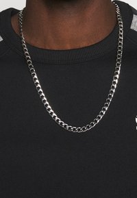 Black sweatshirt with a ribbed collar, featuring a silver chain necklace laid across the fabric, highlighting a smooth, textured appearance.