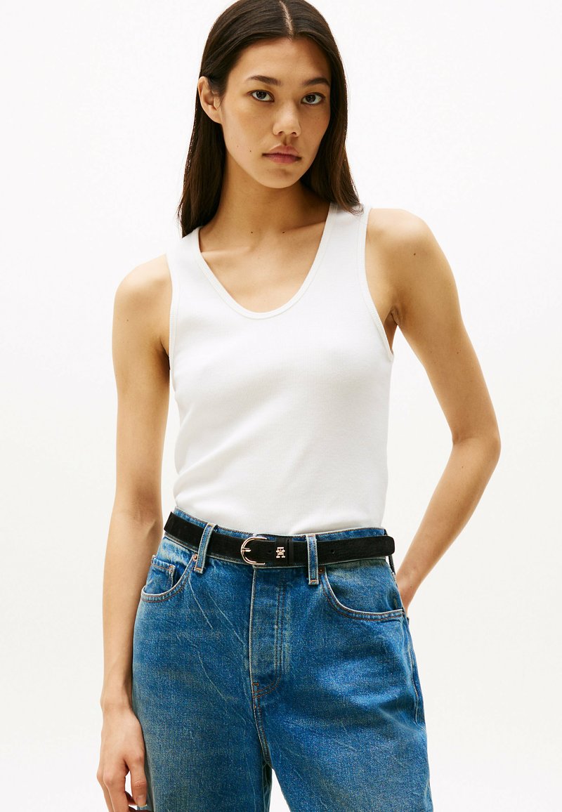 Weißes, geripptes Trägershirt kombiniert mit hochtaillierten blauen Jeans und einem schwarzen, taillierten Gürtel. Das Trägershirt hat einen runden Ausschnitt und sitzt figurbetont.