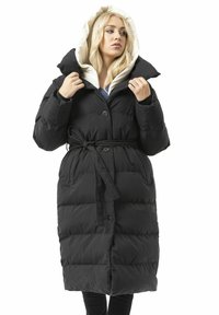 Schwarzer Steppmantel mit tailliertem Schnitt, übergroßem Kragen und hellfarbiger Kapuze. Verfügt über Knopfverschlüsse und horizontale Steppnähte.