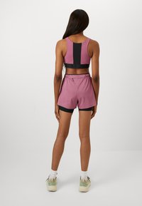 Purple sports bra with black accents, paired with pink shorts. Fabric appears smooth, featuring a drawstring. Sneakers are light green.