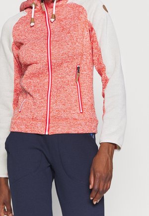 Rot-weißer Kapuzenpullover mit Reißverschluss und Fronttaschen, getragen mit dunkelblauer Hose, gezeigt vom mittleren Oberkörper bis zur Hand vor einem einfarbigen Hintergrund.