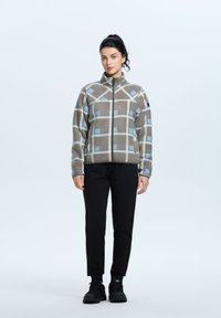 Kurtka polarowa w brązowo-szarym kratę z niebieskimi akcentami; pełny zamek, stójka i elastyczne mankiety. Czarnie spodnie i obuwie dopełniają całość.