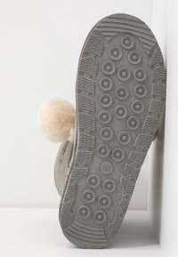 Semelle de botte grise avec des picots en caoutchouc arrondis et un motif texturé. Le côté comporte un accent pompon beige clair, taille indiquée comme 37.