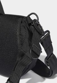 Svart axelväska med en nätpanel på sidan, justerbara remmar och plastdetaljer. Strukturerad tyg med sömnadsdetaljer.