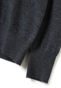 Manica e orlo di un maglione di lana grigio scuro, con polsini a coste e uno spacco laterale su uno sfondo bianco.