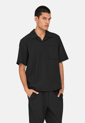 Cămașă neagră cu mâneci scurte, cu guler și buzunar. Textură netedă și croială lejeră, având un design minimalist și linii curate.