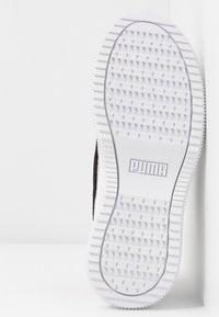 Mustat lenkkarit, joissa on valkoinen kumipohja, jossa on teksturoitu pito kuvio ja harmaa "PUMA"-logo pohjan keskellä.