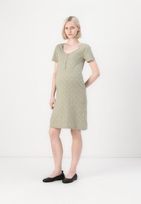 Grūtniecības kleita no mīksta zaļa auduma ar baltām punktiņām, īsām piedurknēm, apaļu dekoltē un līdz ceļiem garu malu. Melni plakanie apavi.