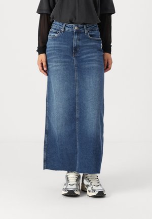 Fustă maxi din denim de culoare albastru închis, cu croială dreaptă, fente în față și tiv brut. Asortată cu adidași argintii și un top negru.