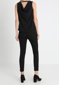 Haut noir sans manches avec un dos drapé, associé à un pantalon noir ajusté et des chaussures à talons hauts noires ; un design lisse et élégant.