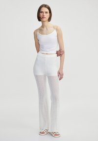 Witte mouwloze top gecombineerd met witte uitlopende haakbroek. Zachte, lichte stof met een gestructureerd patroon. Casual schoeisel maakt de look compleet.
