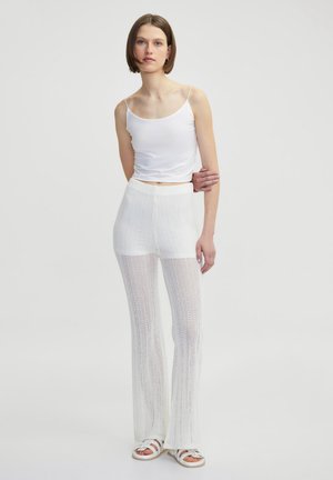 Witte mouwloze top gecombineerd met witte uitlopende haakbroek. Zachte, lichte stof met een gestructureerd patroon. Casual schoeisel maakt de look compleet.