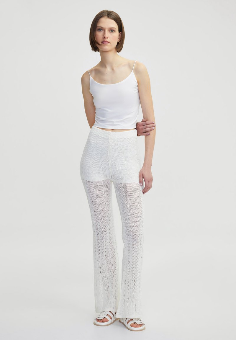 Witte mouwloze top gecombineerd met witte uitlopende haakbroek. Zachte, lichte stof met een gestructureerd patroon. Casual schoeisel maakt de look compleet.
