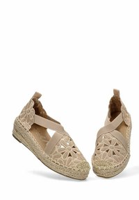 Zapatos tipo espadrille beige con diseño de encaje floral, tiras elásticas cruzadas y suela de cuña envuelta en yute. Estilo de punta abierta con un acabado texturizado.