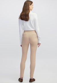 Beige, hoge taillebroek met een slank model en achterzakken, gecombineerd met een wit langpoloshirt en zwart patroon-schoenen.