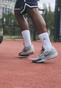 Szare buty do koszykówki Nike z czarnymi akcentami i teksturowaną siateczką u góry, w połączeniu z białymi skarpetkami sportowymi z czarnym logo.