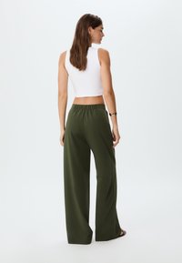 Weißes ärmelloses Crop-Top kombiniert mit lockeren, olivgrünen weit geschnittenen Hosen. Die Hosen verfügen über einen elastischen Bund und eine glatte Textur.